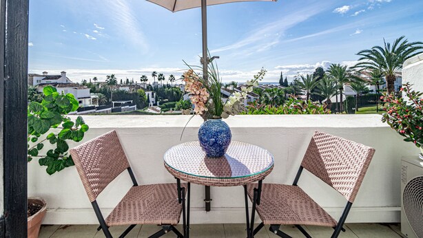 A balcony with a round table, two wicker chairs, a blue vase with flowers, and a beige umbrella. - MA - Elegant Apartment With Sea Views (Marbella)