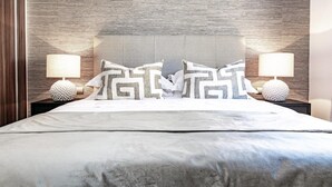 Una cama bien hecha con un cabecero gris, dos lámparas de noche y almohadones decorativos.
