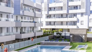 Un moderno edificio de apartamentos con zona de piscina en la azotea, que incluye piscina y sillones de descanso.
