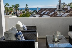 A balcony with wicker furniture, a glass table, and a view of the sea and buildings. - Eld1-stunning 2 Bedroom Penthouse in Puerto Banus (Marbella)