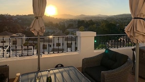 A balcony with wicker furniture, a table with a glass, and two umbrellas. - Ap128 - Big Townhouse - Sunny Side of Aloha Pueblo (Marbella)