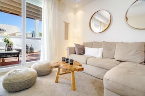 A living room with a sofa, round mirrors, a wooden coffee table, and a view of the outside. - Ar23 - Holiday Flat, Puerto Banus by Roomservices (Marbella)