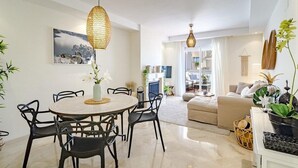 A modern living room with a round dining table, black chairs, a sofa, and a TV. - Ar23 - Holiday Flat, Puerto Banus by Roomservices (Marbella)