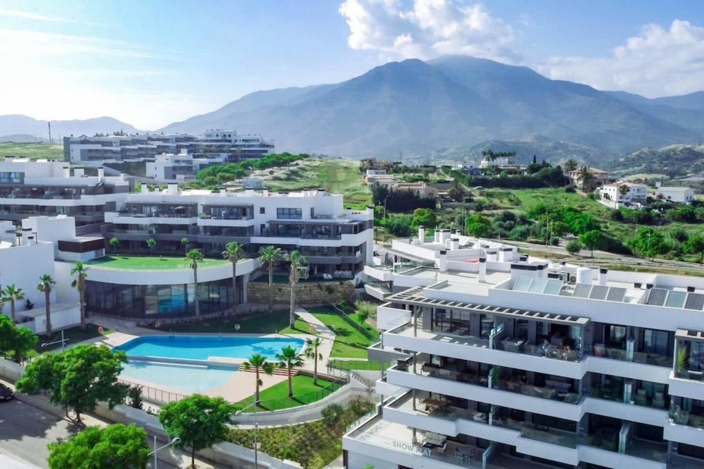 A modern hotel with multiple buildings, a swimming pool, and a mountainous backdrop.
