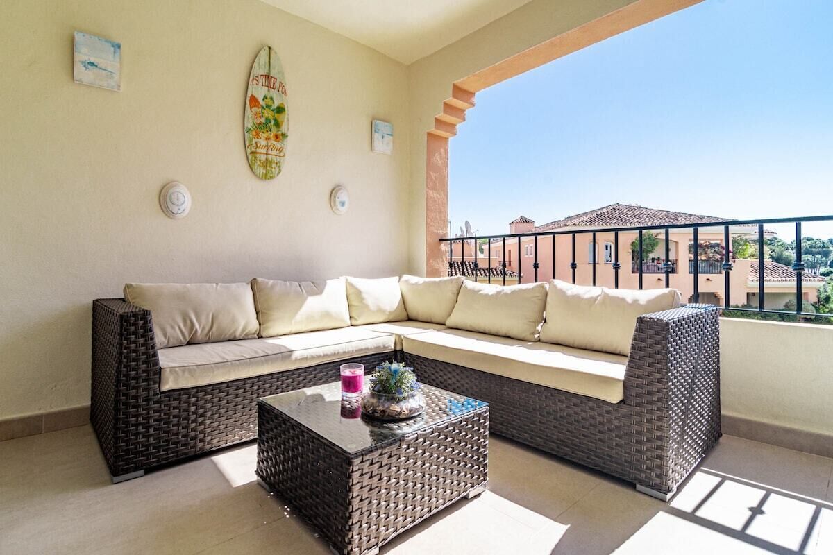 A balcony with a wicker sofa, a glass coffee table, and a view of buildings.