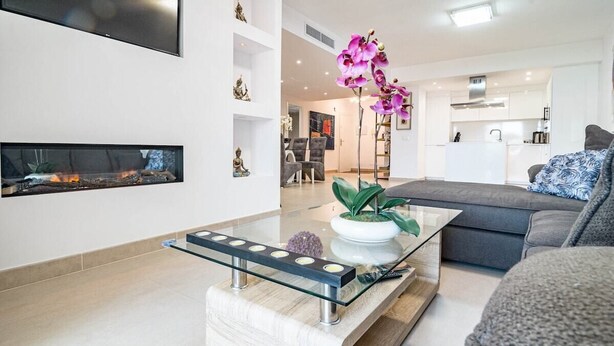 A modern living room with a glass coffee table, a fireplace, and a kitchen in the background. - Cpg- Perfect Holiday Home Close to Puerto Banus (Marbella)
