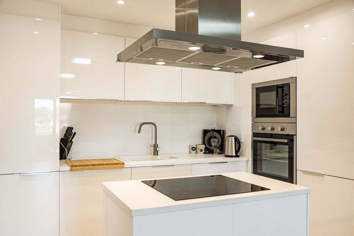 A modern kitchen with white cabinetry, a stainless steel range hood, a built-in microwave, and an oven.