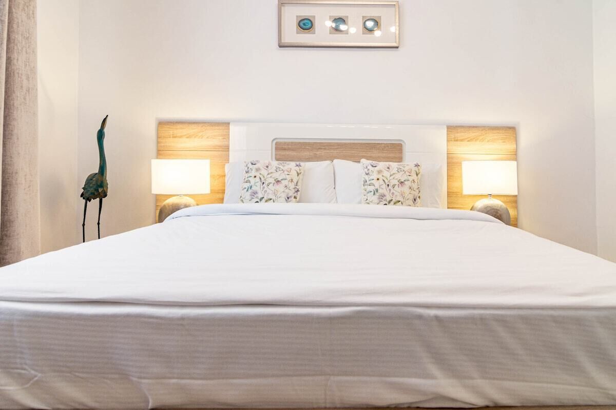 Un lit bien fait, avec une tête de lit en bois, deux lampes de chevet et un élément décoratif accroché au mur au-dessus.