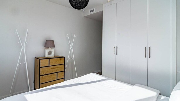 A bedroom with a bed, a wardrobe, a dresser, and two white abstract wall decorations. - Lmt46 - Modern Style Spacious Townhouse (Estepona)
