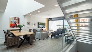 A modern living room with a dining area, a staircase, and large windows. - Lmt46 - Modern Style Spacious Townhouse (Estepona)