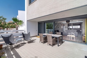 A modern outdoor patio with a dining table and chairs, a glass door leading to a living area, and a white building with a brick facade. - Lmt46 - Modern Style Spacious Townhouse (Estepona)