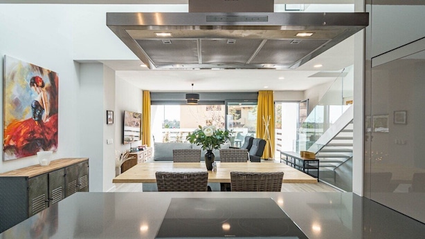 A modern kitchen with a large island, a dining area with wicker chairs, and a view of the outdoors through large windows. - Lmt46 - Modern Style Spacious Townhouse (Estepona)