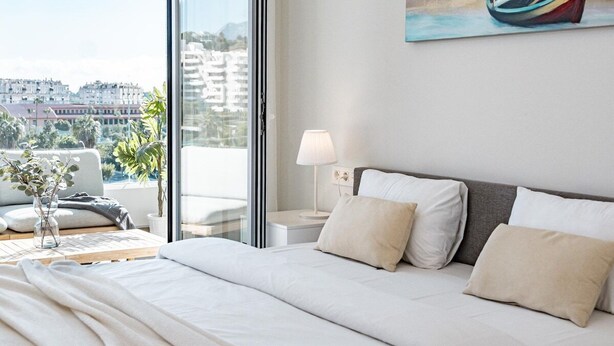 A modern hotel room with a large bed, a nightstand, a lamp, and a painting of a boat on the wall. - JG- Top Modern Apartment in Nueva Andalucia (Marbella)