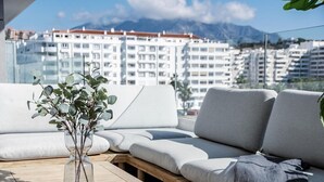 A modern outdoor seating area with a clear view of a cityscape and mountains in the background. - JG- Top Modern Apartment in Nueva Andalucia (Marbella)