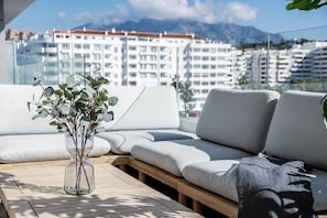 Un espace extérieur moderne, aménagé pour se détendre, offrant une vue dégagée sur le paysage urbain et les montagnes en arrière-plan.