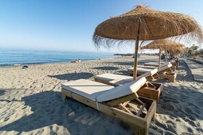 A beach with wooden lounge chairs and thatched umbrellas. - JG- Top Modern Apartment in Nueva Andalucia (Marbella)