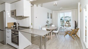 A modern kitchen with white cabinetry, a built-in oven, and a dining area with a round table and chairs. - JG- Top Modern Apartment in Nueva Andalucia (Marbella)