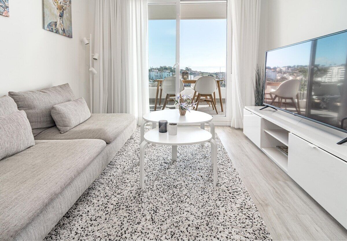 Ein modernes Wohnzimmer mit einer Couch, einem Couchtisch, einem Fernseher und einem Balkon mit Blick.