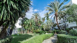 Un jardín bien cuidado con un sendero de piedra, palmeras y setos ordenados.