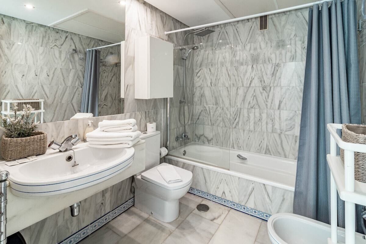 Un bagno moderno con una parete in marmo, una vasca, un water e un lavabo.
