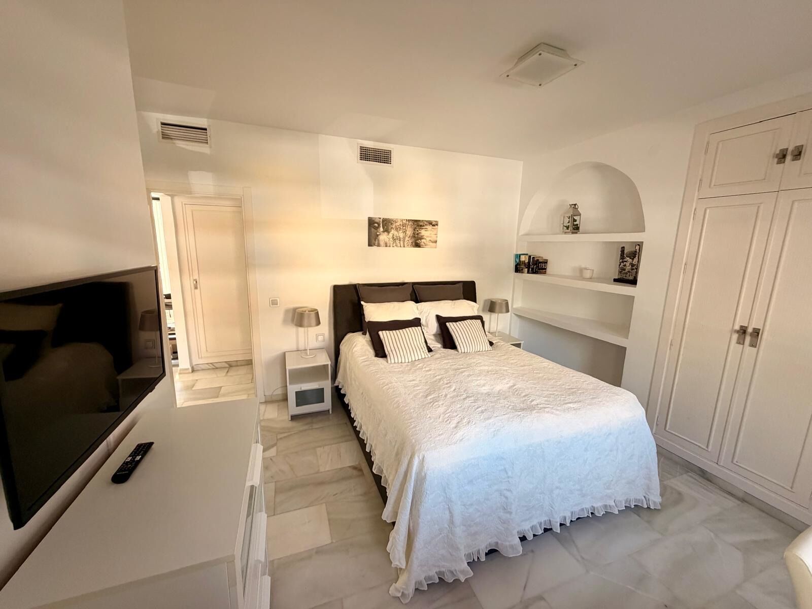 A bedroom with a bed, bedside tables, a TV, and a wardrobe.