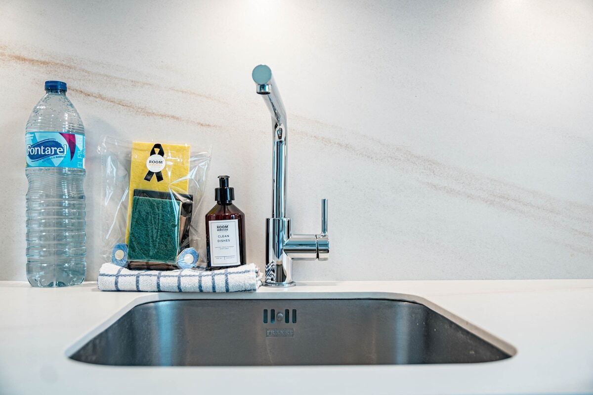A kitchen sink with a faucet, a bottle of water, a sponge, a bottle of dish soap, and a towel.