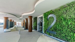 Eine moderne Hotellobby mit gewölbter Decke, großen Säulen und einer vertikalen Grünwand mit einem auffälligen Schild mit der Zahl '2'.