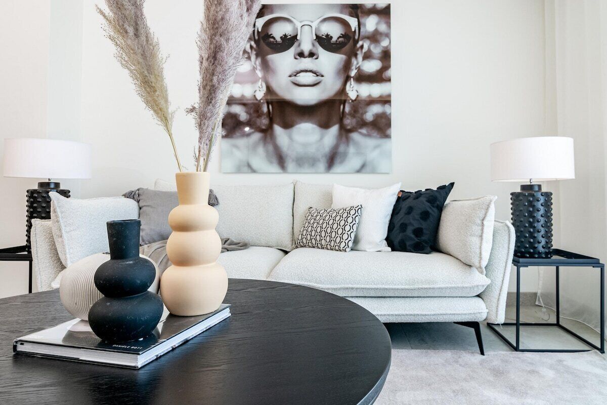 A modern living room with a sofa, two side tables with lamps, a coffee table with decorative items, and a large wall art piece.