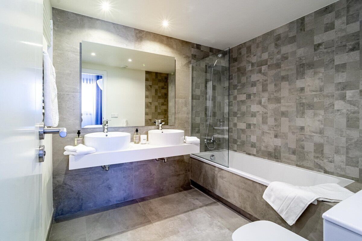 Een moderne badkamer met een dubbele wastafel, een douchecabine van glas en een bad.
