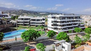 Un immeuble d’appartements moderne doté de nombreux balcons, d’une piscine et offrant une vue sur la ville et les montagnes en arrière-plan.