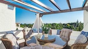 Eine Dachterrasse mit Korbmöbeln, einem Glastisch und Blick auf Grünflächen und Gebäude.