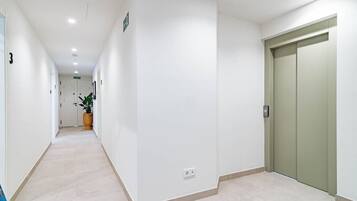 Un pasillo limpio y moderno con piso de baldosas, una planta en maceta y una puerta cerrada.