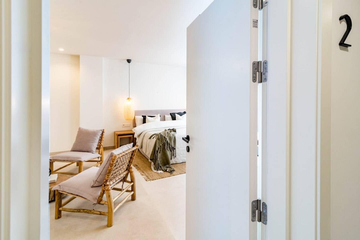 A hotel room with a bed, two chairs, a nightstand, and a hanging light fixture.