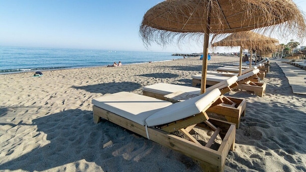 Une plage avec des chaises longues en bois et des parasols en chaume.