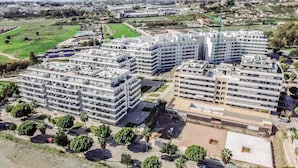 Un immeuble résidentiel moderne à plusieurs étages, doté d’un toit plat, entouré de verdure et comprenant un espace de stationnement.