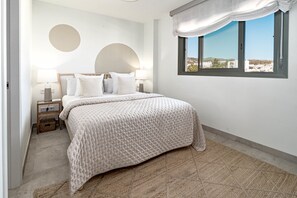 A bedroom with a bed, two bedside tables, a window with a view, and a wall with two circular decorations. - Inf2.4e - Modern 2-bed Apt With Roof top Pool (Estepona)