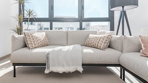 A modern living room with a sectional sofa, patterned cushions, a throw blanket, a floor lamp, and a large window with a view of buildings. - Eg54a - Luxury Penthouse With Private sun Terrace (Estepona)