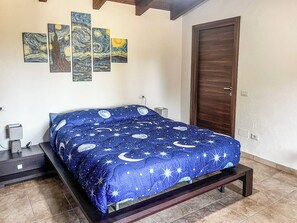 Un dormitorio con una cama, una mesita de noche, una puerta de madera y una pared con cuatro cuadros.
