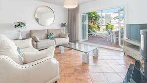 A modern living room with a sofa, a glass coffee table, and a TV. There is a balcony with outdoor furniture. - PG9 - Andalucian 3-story Townhouse Near Estepona (Estepona)