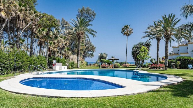 A swimming pool with a curved edge, surrounded by well-maintained grass and palm trees. - PG9 - Andalucian 3-story Townhouse Near Estepona (Estepona)