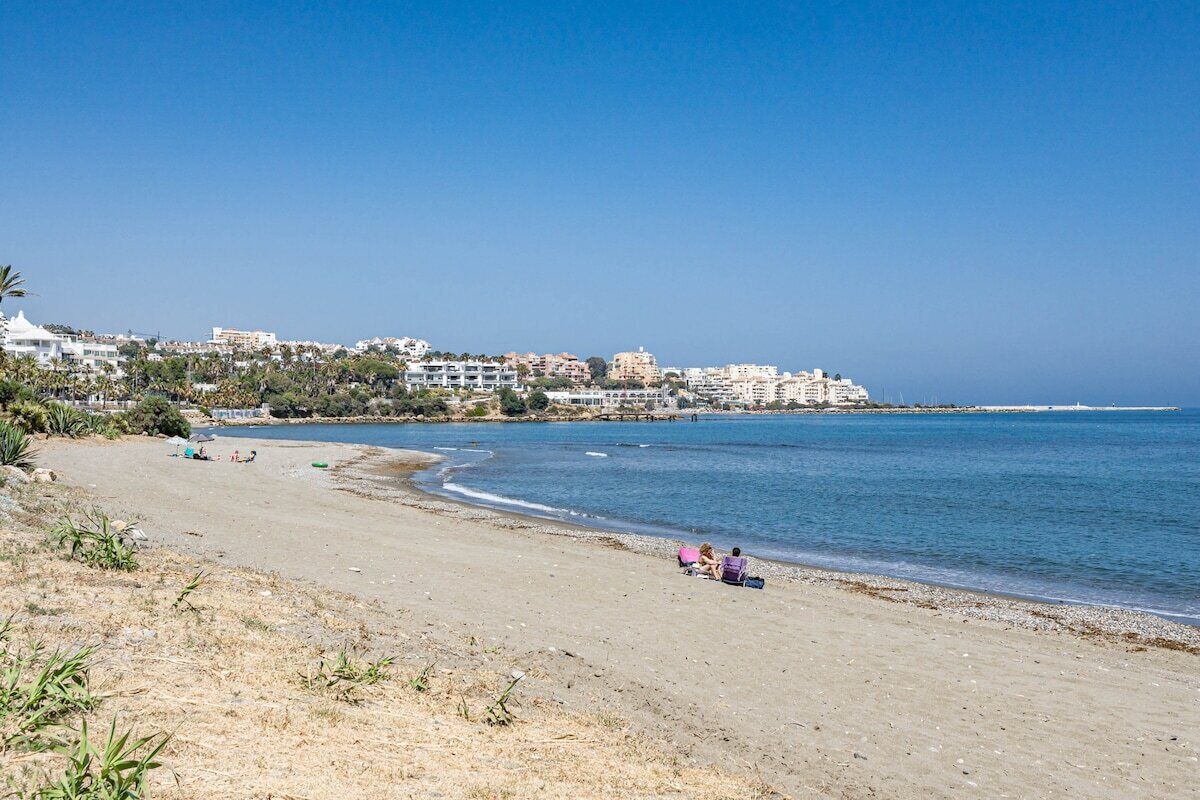 Ein Strand mit freiem Blick auf das Meer, sandigem Ufer und Gebäuden im Hintergrund.