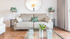 A living room with a sofa, two side tables with lamps, a coffee table, and a large mirror on the wall. - PG9 - Andalucian 3-story Townhouse Near Estepona (Estepona)
