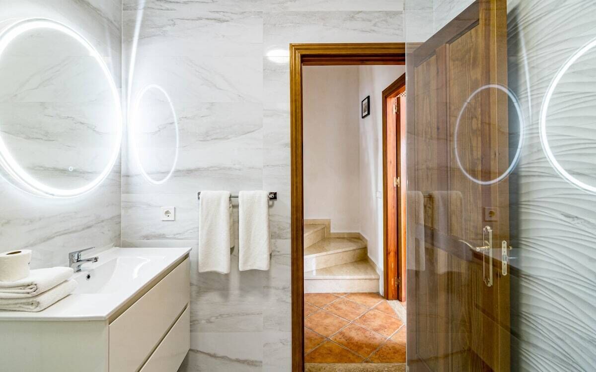 A modern bathroom with a marble wall, a sink with a mirror, and a wooden door leading to a staircase.