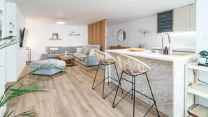 A modern kitchen with a white countertop, two bar stools, a wooden dining table, and a grey sofa. - Eac3f- Modern & Light Apartment Steps From the sea (Estepona)