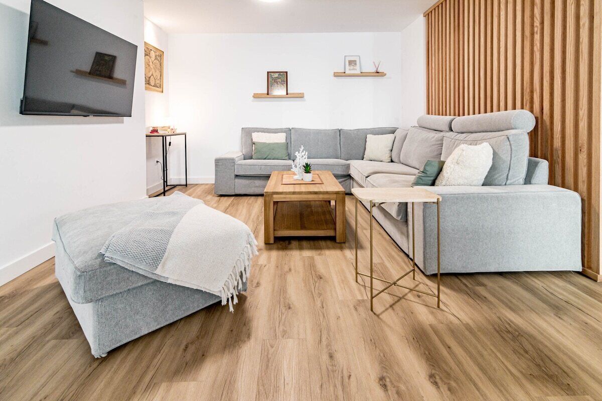 Un salon moderne avec un canapé gris, une table basse en bois et un téléviseur fixé au mur.