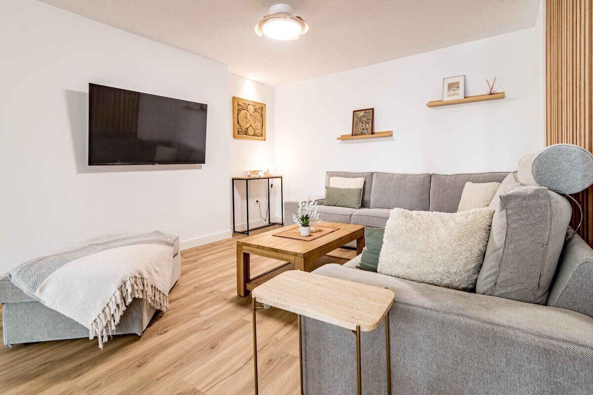 Una sala de estar moderna con un sofá gris, una mesa de centro de madera y un televisor montado en la pared.