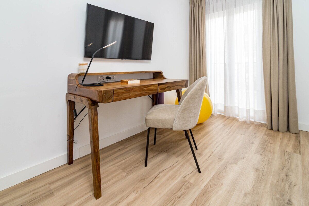 Une chambre moderne avec un bureau en bois, une chaise, un téléviseur à écran plat et une fenêtre avec des rideaux.