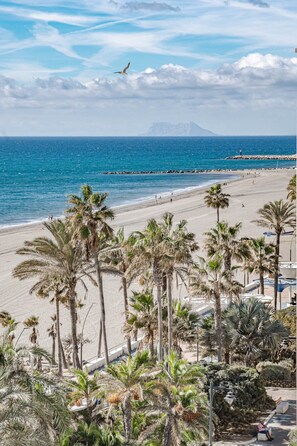 A beach with palm trees, a rocky breakwater, and a clear view of the ocean. - Eac3f- Modern & Light Apartment Steps From the sea (Estepona)
