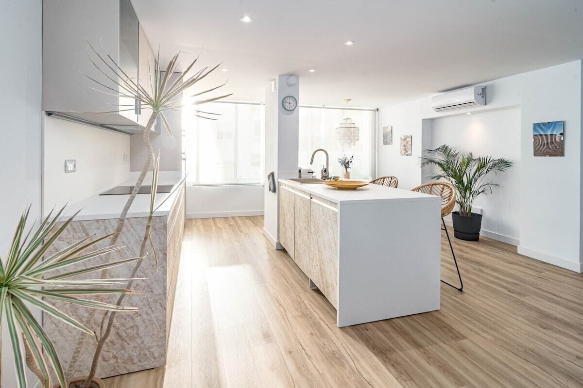 A modern kitchen with a central island, wooden flooring, and potted plants.