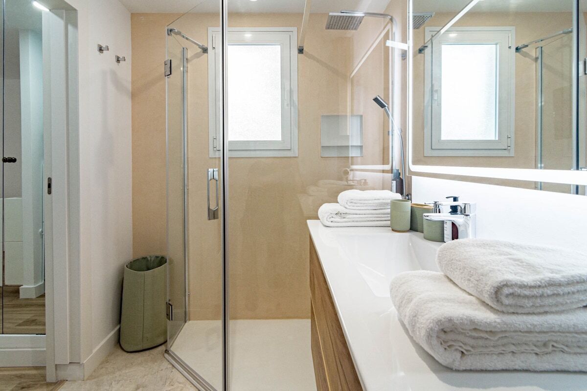 A modern bathroom with a glass shower enclosure, a large mirror, and a vanity with towels.